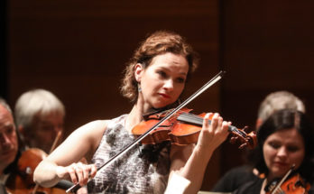 Violinist Hilary Hahn performing in front of an orchestra.