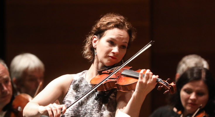 Violinist Hilary Hahn performing in front of an orchestra.